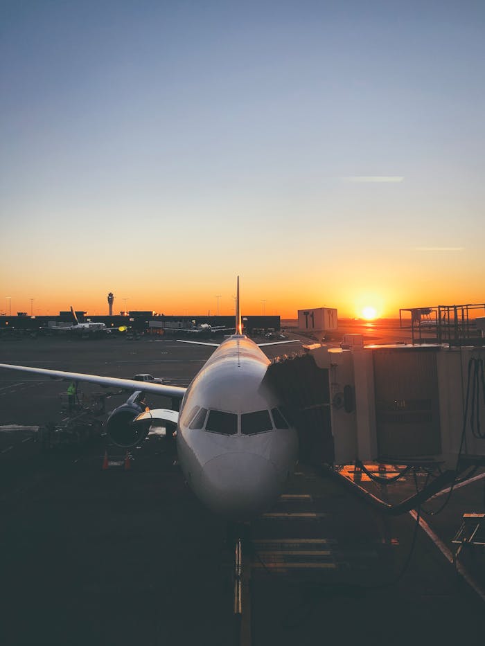 our-story A commercial airplane docked at an airport gate as the sun rises, casting a golden glow.